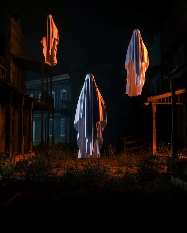 Tre volti spettrali avvolti in lenzuola bianche fluttuano in un paesaggio notturno desolato.