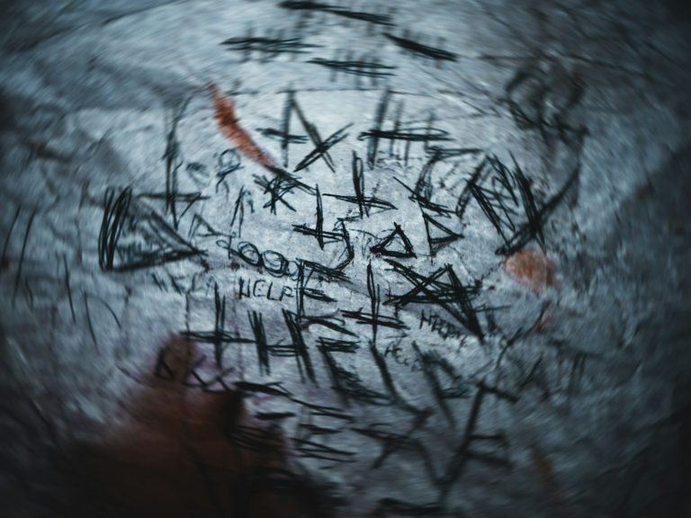 Segni e simboli scolpiti su una superficie scura, con segni di ossido e macchie rosse.