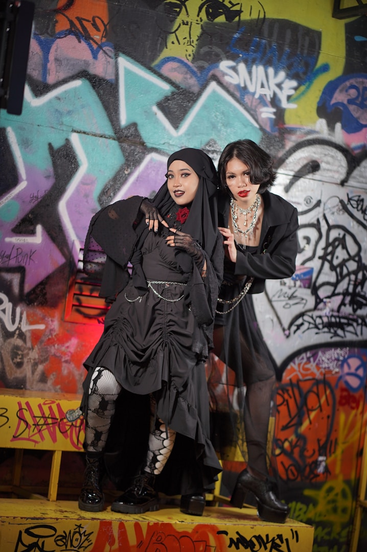 Due donne in abbigliamento alternativo posano davanti a un muro di graffiti colorato.