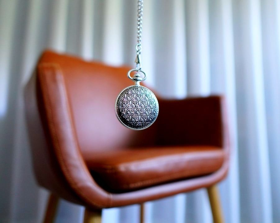 Pendolo ipnosi con pendente sferico, appesa vicino a una sedia in pelle arancione.