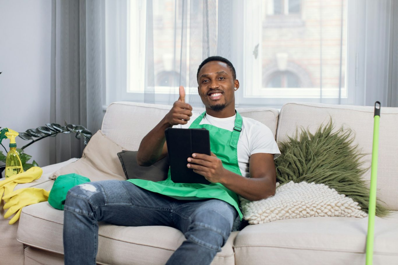 A man in an green apron smiles and gives a thumbs up while holding a tablet.