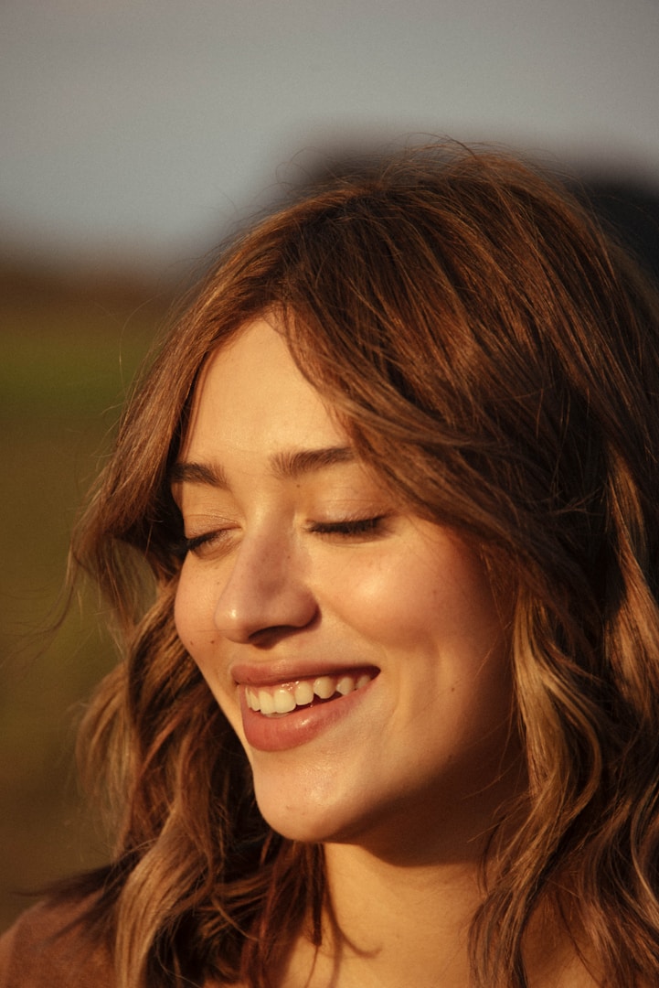 Giovane donna sorridente con i capelli castani in un ambiente all'aperto.