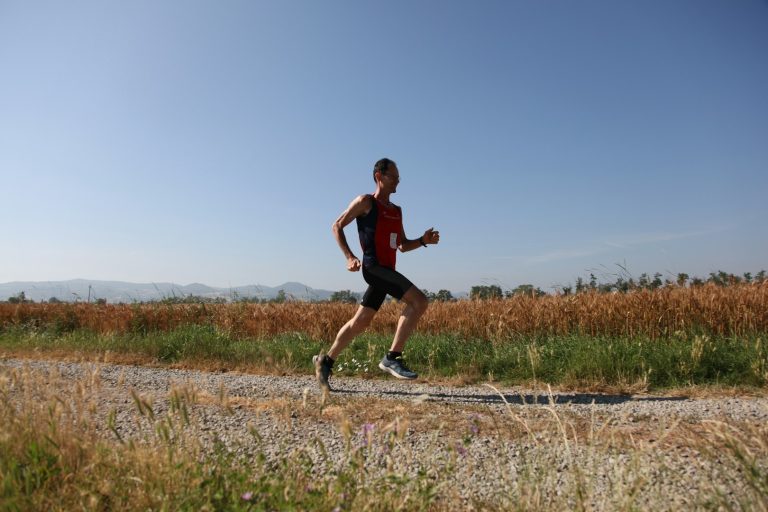 A person running on a gravel path surrounded by grass and distant mountains.