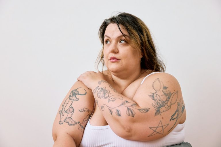 Donna obesa con capelli lunghi e tatuaggi su entrambe le braccia, sguardo serio.