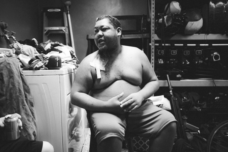 Uomo senza maglietta in sovrappeso, seduto su sedia