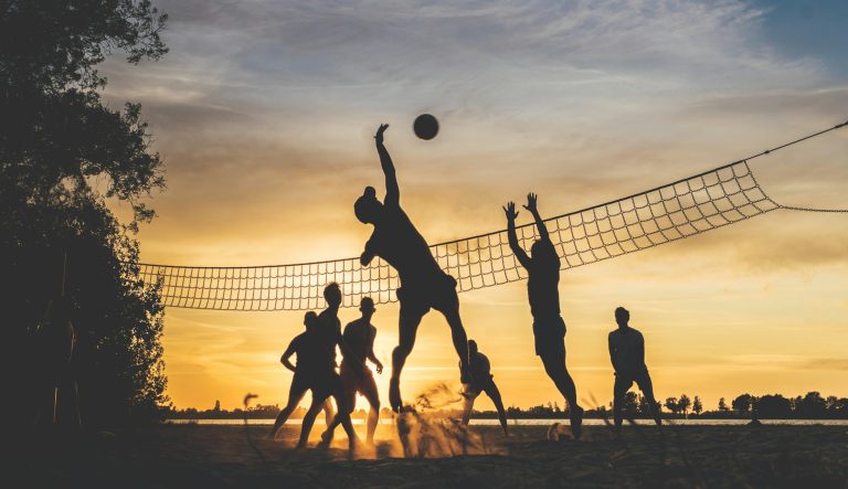 Silhouette of people playing beach volleyball against a sunset backdrop.