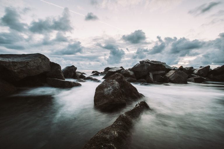 Rocks in shallow water under a cloudy sky at dusk.